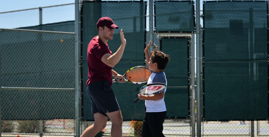 Photo of a kid high fiving his trainer at the Pass Kids tennis event.